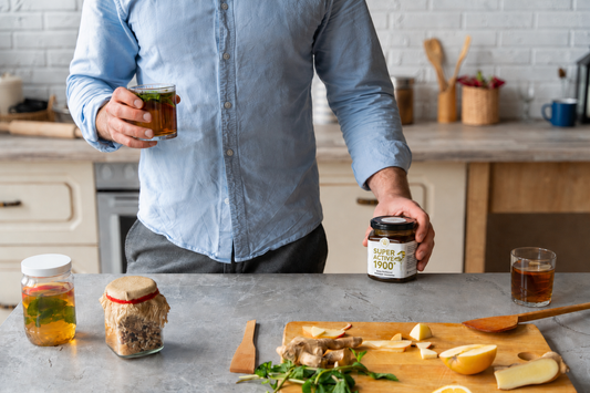 Man preparing herbal tea in a bright kitchen while checking a small Reformwelt Super Active 1900+ bioactive honey jar on the countertop.
