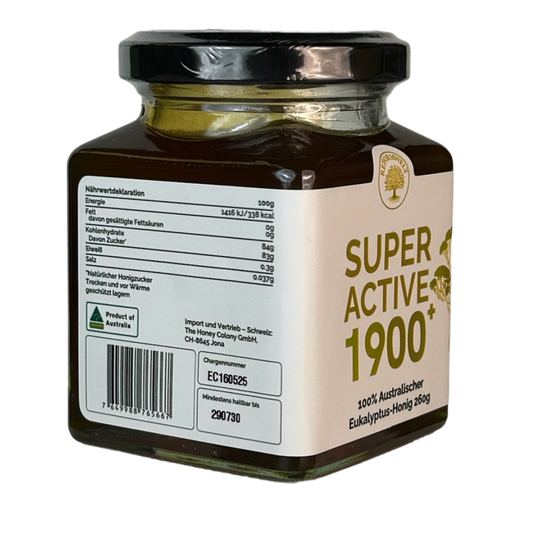 Glass jar of Super Active 1900+ eucalyptus honey shown at an angle, with a cream label and black lid on a transparent background.
